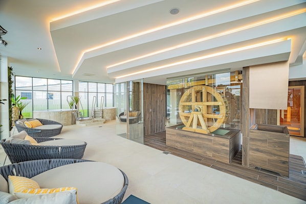 A spacious indoor area with modern furniture, a large wooden wheel structure, and a glass partition.
