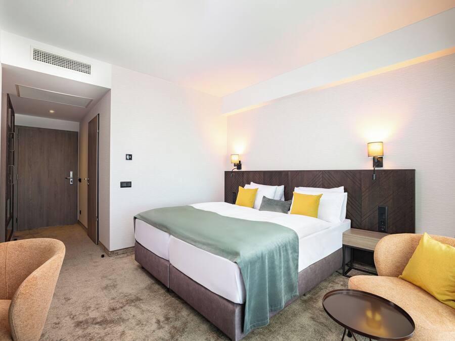 Une chambre d’hôtel comprenant un lit, deux lampes de chevet, un canapé, une petite table et une porte donnant sur un couloir.