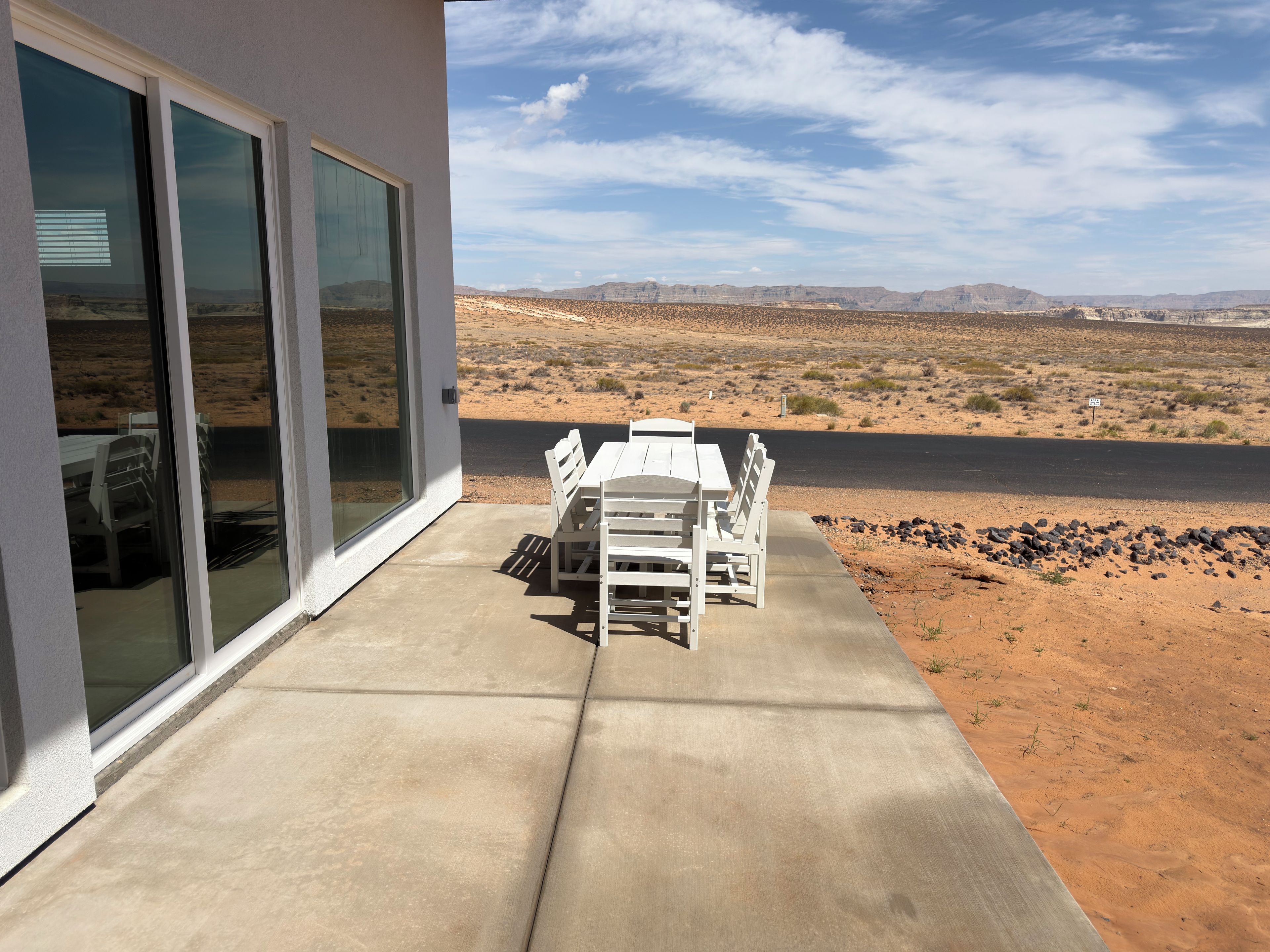 Een terras met een tafel en stoelen, uitzicht op een woestijnlandschap en een waterpartij in de verte.