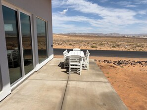 Eine Terrasse mit Tisch und Stühlen, Blick auf eine Wüstenlandschaft und ein Gewässer in der Ferne.