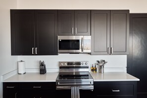 Eine moderne Küche mit dunklen Schränken, einer Edelstahl-Mikrowelle, einem Backofen und einem Kochfeld.