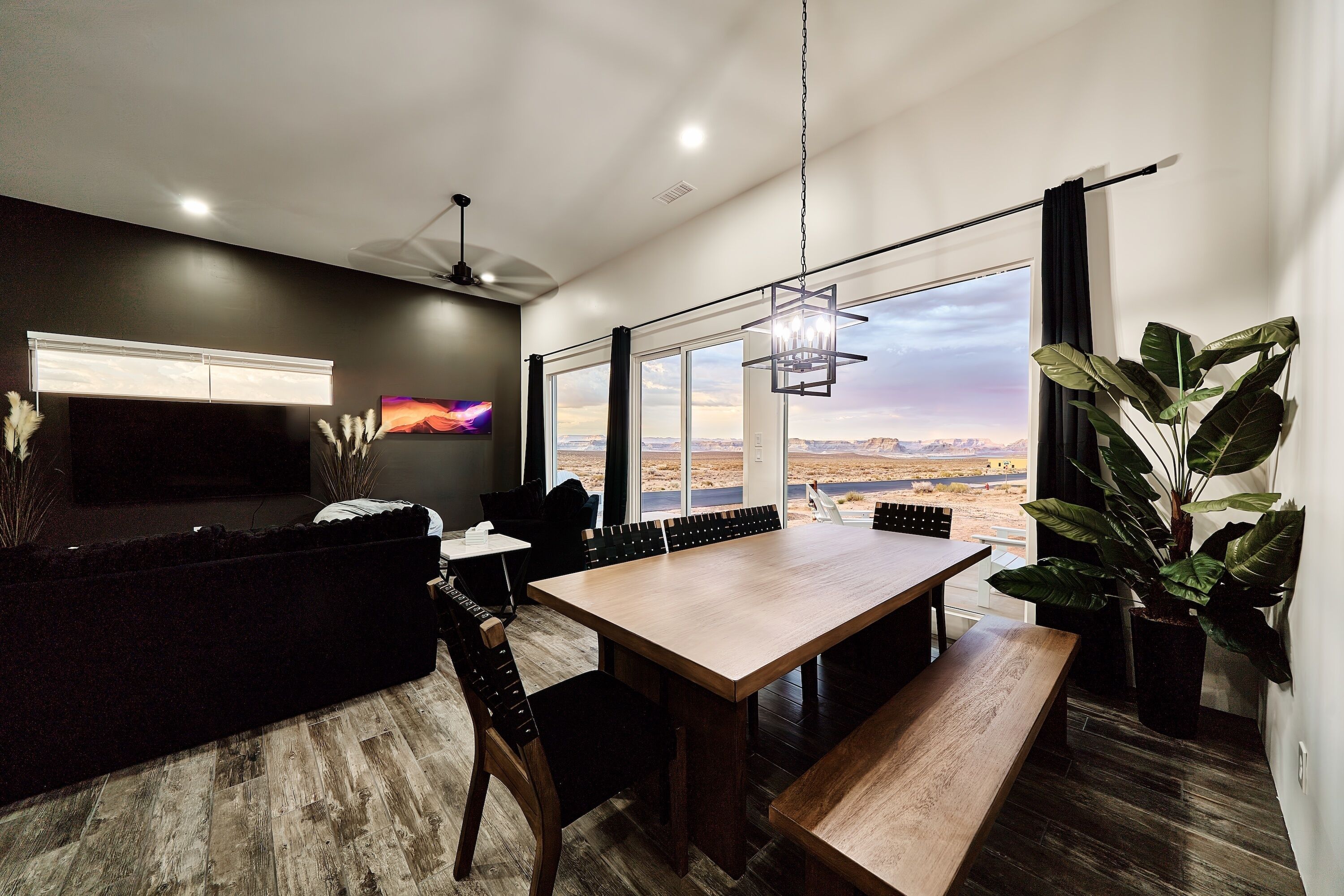 A modern living room with a large window, a flat-screen TV, and a dining area with a wooden table and chairs.
