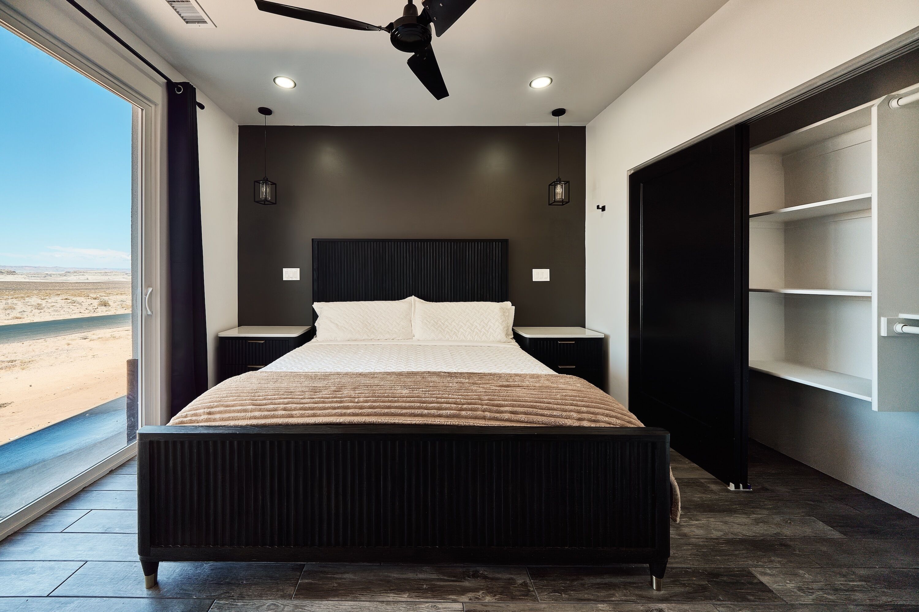 A modern bedroom with a large bed, a ceiling fan, and a view of the desert through a large window.
