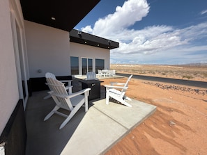 A patio with white Adirondack chairs and a black table, overlooking a desert landscape.