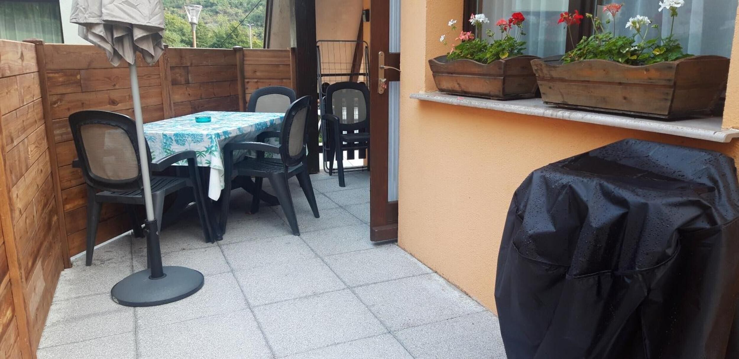Un espace patio avec une table et des chaises, un barbecue et des jardinières sur un balcon.