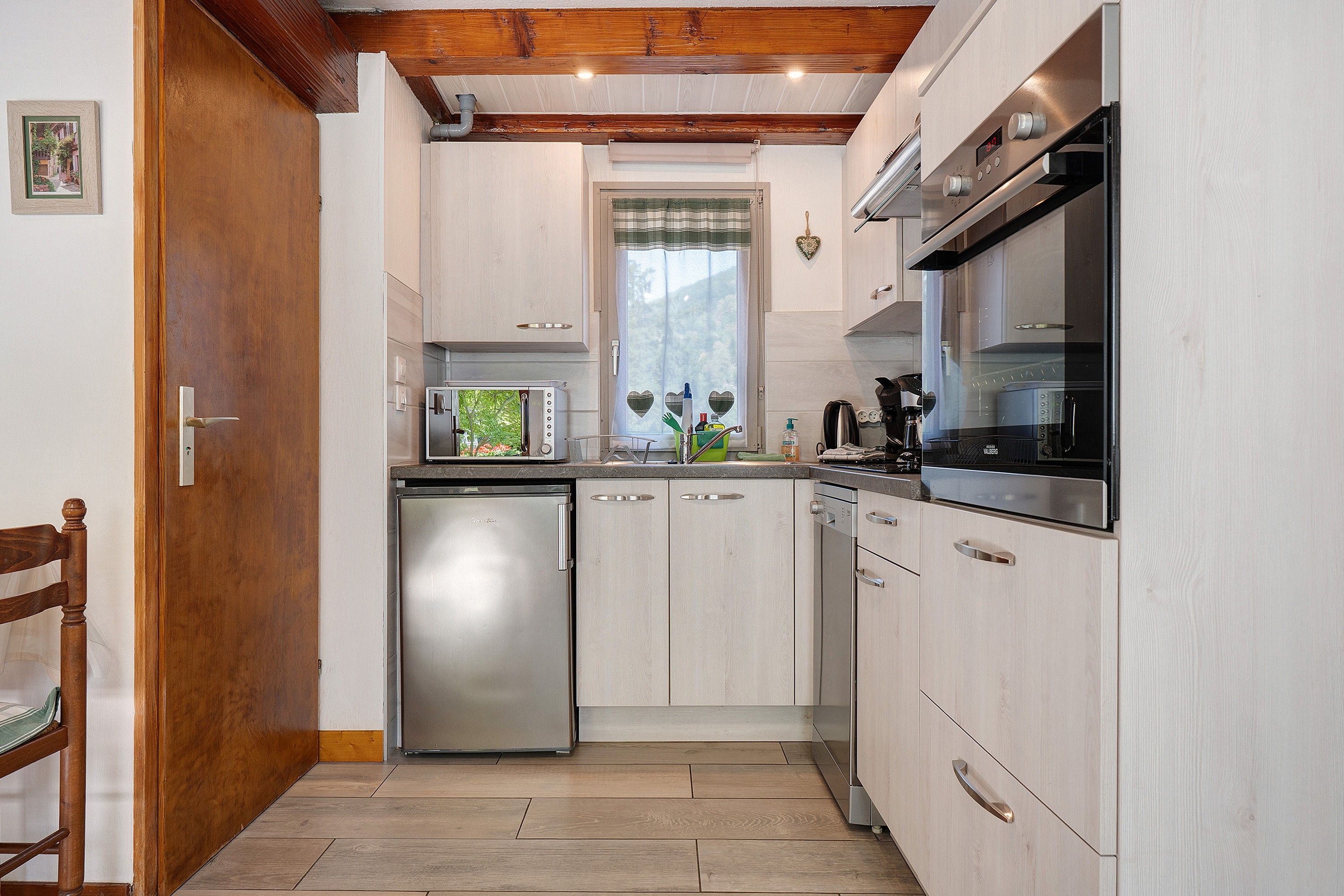 A modern kitchen with stainless steel appliances, wooden cabinetry, and a window with heart-shaped cutouts.