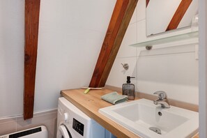 Un baño pequeño con tocador de madera, lavadora y lavamanos.