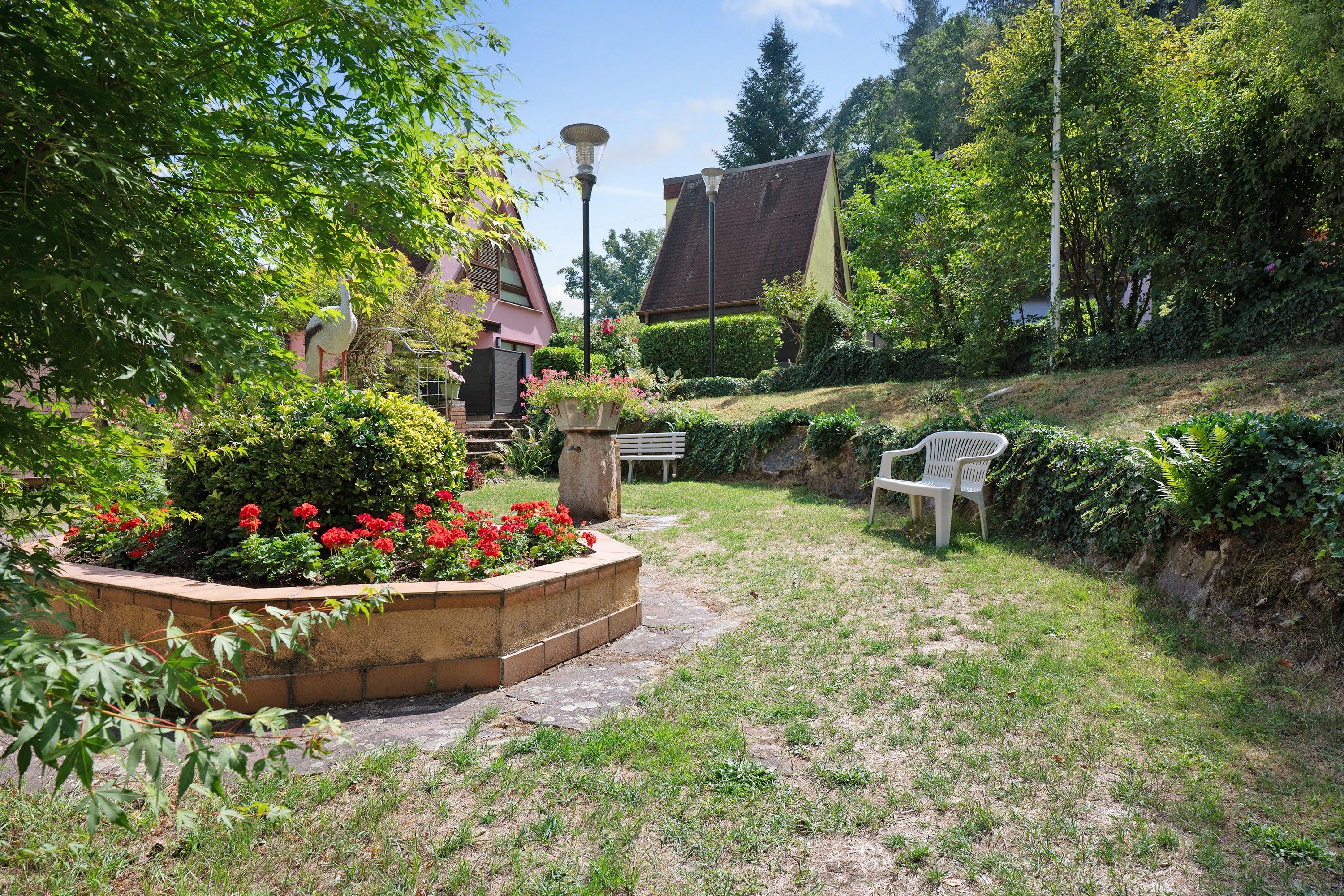 A landscaped garden with a bench, a lamp post, and a bird sculpture.