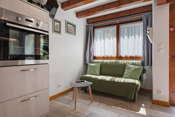 A compact kitchen with a built-in oven, a small table, and a green sofa by a window with curtains.