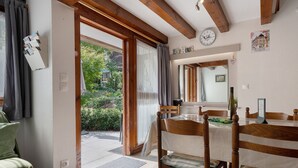 Un coin repas avec une table et des chaises en bois, une horloge au mur et une vue sur un jardin par la porte ouverte.