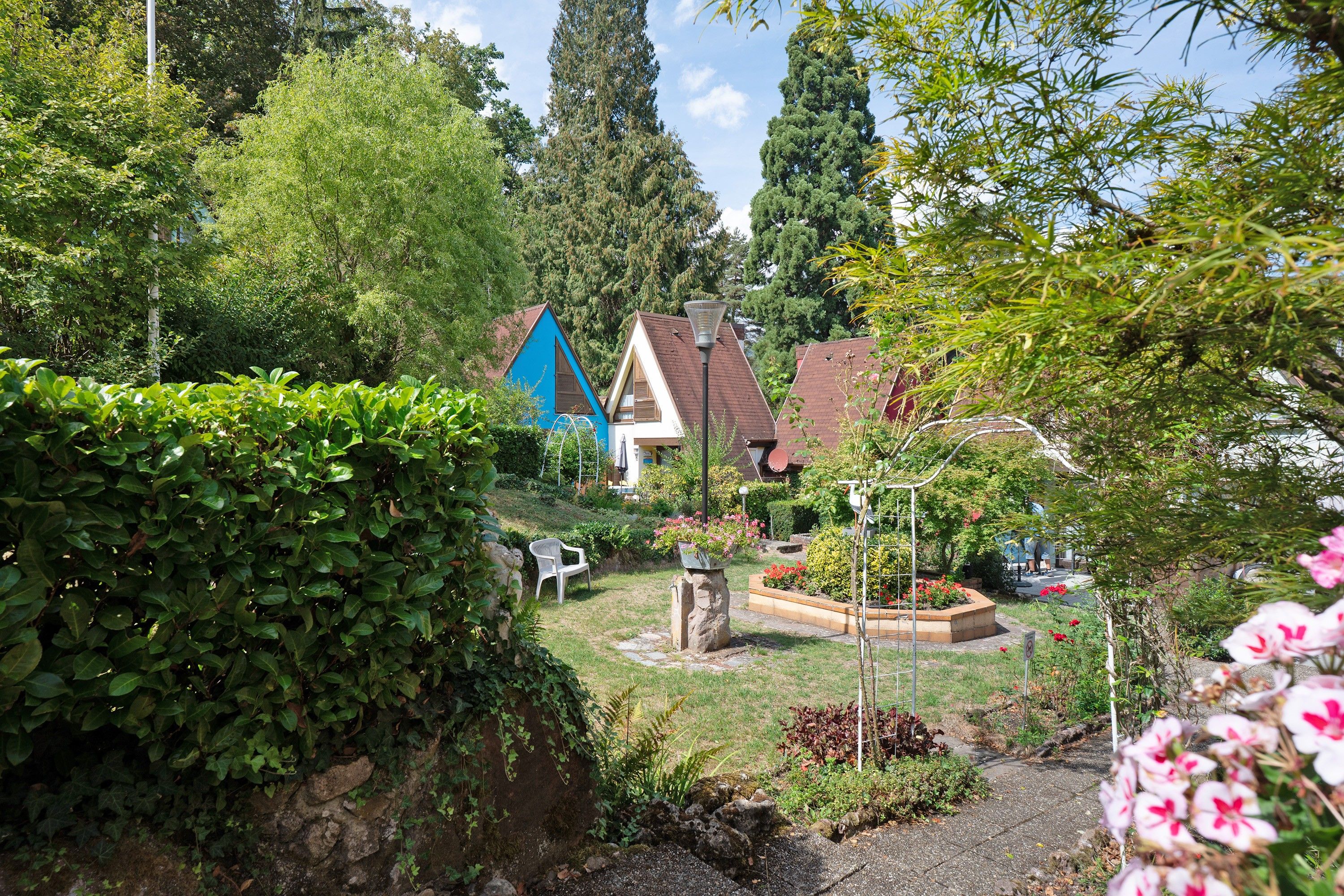 A residential area with houses, a garden with a bench, and a stone wall.