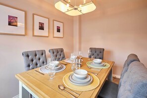 Une salle à manger avec une table en bois dressée pour quatre personnes, des chaises à revêtement gris et des tableaux encadrés accrochés au mur.