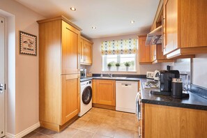 A modern kitchen with wooden cabinets, a washing machine, a dishwasher, and a coffee machine. - Host & Stay | Stratton Close (Brotton)