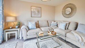 Ett modernt vardagsrum med en beige soffa, ett soffbord i glas och en dekorativ spegel.