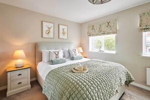 A bedroom with a bed, two bedside lamps, a nightstand, a window with a view, and two framed animal prints on the wall. - Host & Stay | Stratton Close (Brotton)