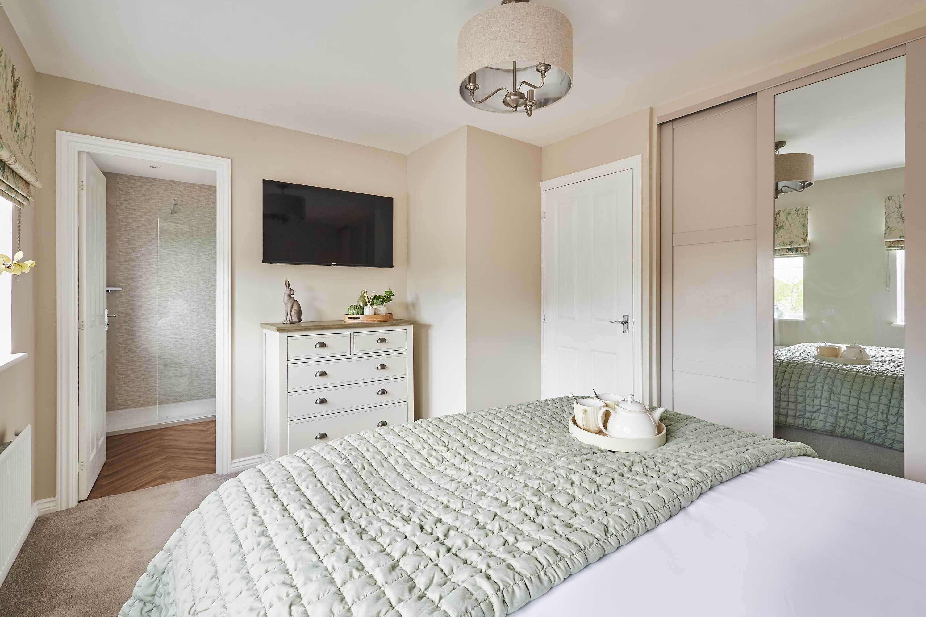 Een slaapkamer met een bed, een kaptafel, een televisie en een deur naar een andere kamer.