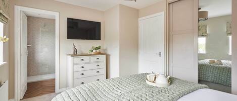 Un dormitorio con cama, cómoda, televisor y puerta que da a otra habitación.