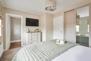 Ein Schlafzimmer mit Bett, Kommode, Fernseher und einer Tür zu einem weiteren Raum.
