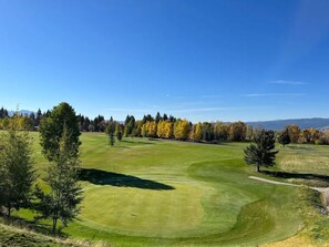 A golf course with a clear sky, trees, and distant mountains.