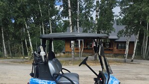 A golf cart parked on a gravel surface with a wooden cabin in the background.