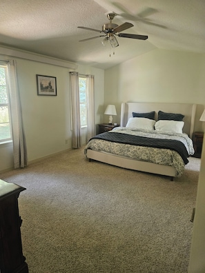 A bedroom with a bed, a ceiling fan, a nightstand, a lamp, and a window with curtains.