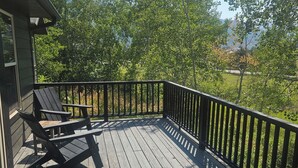 Una terraza de madera con barandilla, un banco y vistas a árboles y un paisaje distante.
