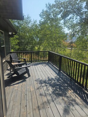 A wooden deck with a railing, a bench, and a view of trees and a distant landscape.