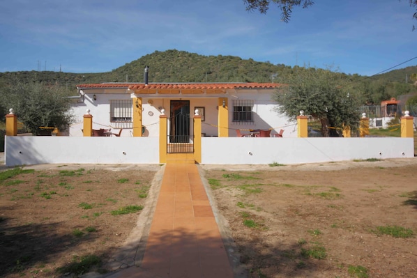 A single-story house with a tiled roof, a front gate, and a paved driveway leading to the entrance.