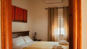 A hotel room with a bed, a nightstand, a window with curtains, and a painting on the wall. - Rural House "Los Naranjo" with Mountain Views, Pool, and Barbecue (Jerez de los Caballeros)