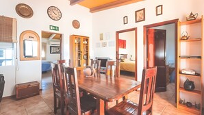 A dining area with a wooden table and chairs, a kitchen in the background, and a hallway leading to a bedroom. - Rural House "Los Naranjo" with Mountain Views, Pool, and Barbecue (Jerez de los Caballeros)