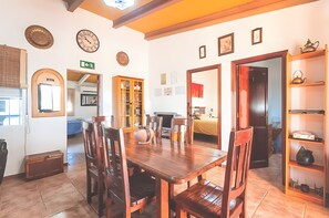 A dining area with a wooden table and chairs, a kitchen in the background, and a hallway leading to a bedroom. - Rural House "Los Naranjo" with Mountain Views, Pool, and Barbecue (Jerez de los Caballeros)