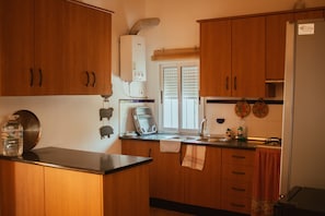 A kitchen with wooden cabinets, a water dispenser, a kettle, and a window with blinds.