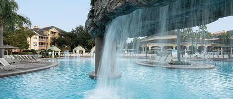 A swimming pool with a waterfall feature, lounge chairs, and a building in the background.
