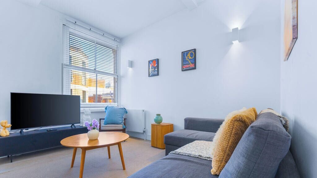 A modern living room with a flat-screen TV, a sofa, a coffee table, and artwork on the walls.
