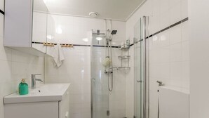 Ett modernt badrum med en duschkabin i glas, en vit tvättställ och en handduksställning.