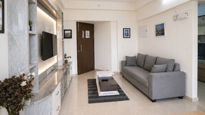 Una sala moderna con un sofá gris, un televisor de pantalla plana montado en una pared de mármol, un ventilador de techo y una mesa de centro de madera.