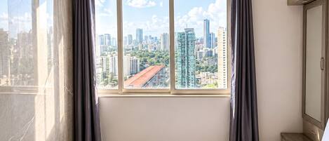 A hotel room with a large window, a bed, a bedside table, and a wardrobe.