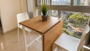 Una habitación moderna con una mesa de madera, dos sillas blancas, una planta en maceta y un ventanal con vistas a la ciudad.