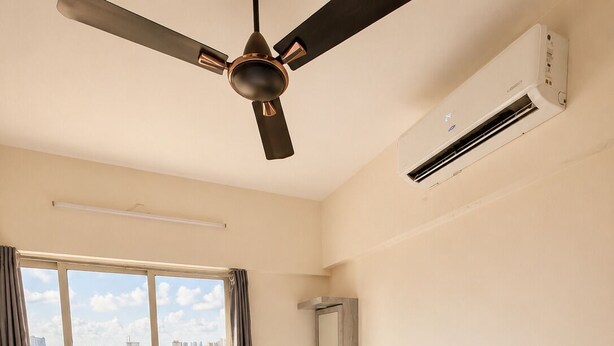 Habitación de hotel con cama, ventilador de techo, unidad de aire acondicionado, ventana con vista a la ciudad y una mesita de noche con un florero.