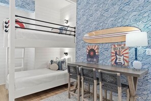 Ein Stockbett mit weißem Kopfteil, ein kleiner Tisch mit Stühlen sowie eine Wand mit Surfbrett- und Gitarren-Kunstwerken.