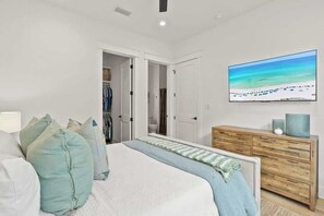 Um quarto com cama, cômoda, televisão e armário.