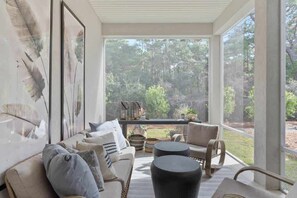 Habitación iluminada por el sol con un sofá, sillas y una mesa de centro, con vistas a un área boscosa.