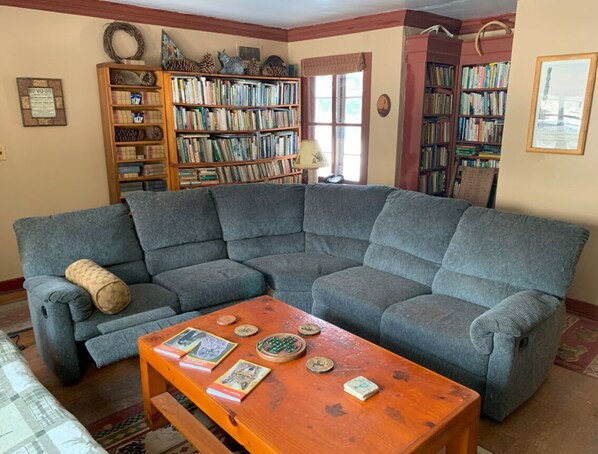 A living room with a sectional sofa, a coffee table with books and decorative items, and two bookshelves filled with books.