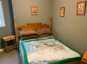 A bedroom with a wooden bed, a quilt with a wolf design, and framed pictures on the wall. - Rustic Ausable Lodge Waterfront (Wilmington)