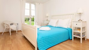 Una camera da letto con un letto, una sedia, un comodino, una lampada e una finestra con tende.