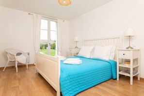 Une chambre à coucher avec un lit, une chaise, une table de chevet, une lampe et une fenêtre avec des rideaux.