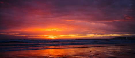 Ein Strand bei Sonnenuntergang mit Wellen und bewölktem Himmel.
