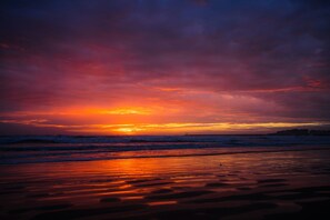 Une plage au coucher du soleil, avec des vagues et un ciel nuageux.