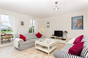 Un salon avec des canapés à rayures, une table basse, un téléviseur et une vue sur l’extérieur.