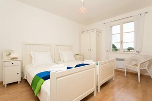 Ein Schlafzimmer mit einem Bett, Nachttischen, einem Kleiderschrank, einem Sessel und einem Fenster mit Vorhängen.
